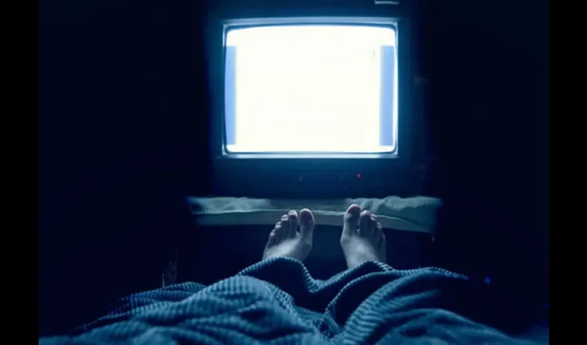Foto ilustrativa de una persona acostada con la televisión encendida. 